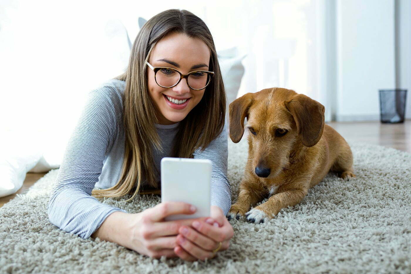 Nainen ja hänen koiransa makaavat yhdessä lattialla karvamatolla ja ottavat selfietä naisen puhelimella Retta